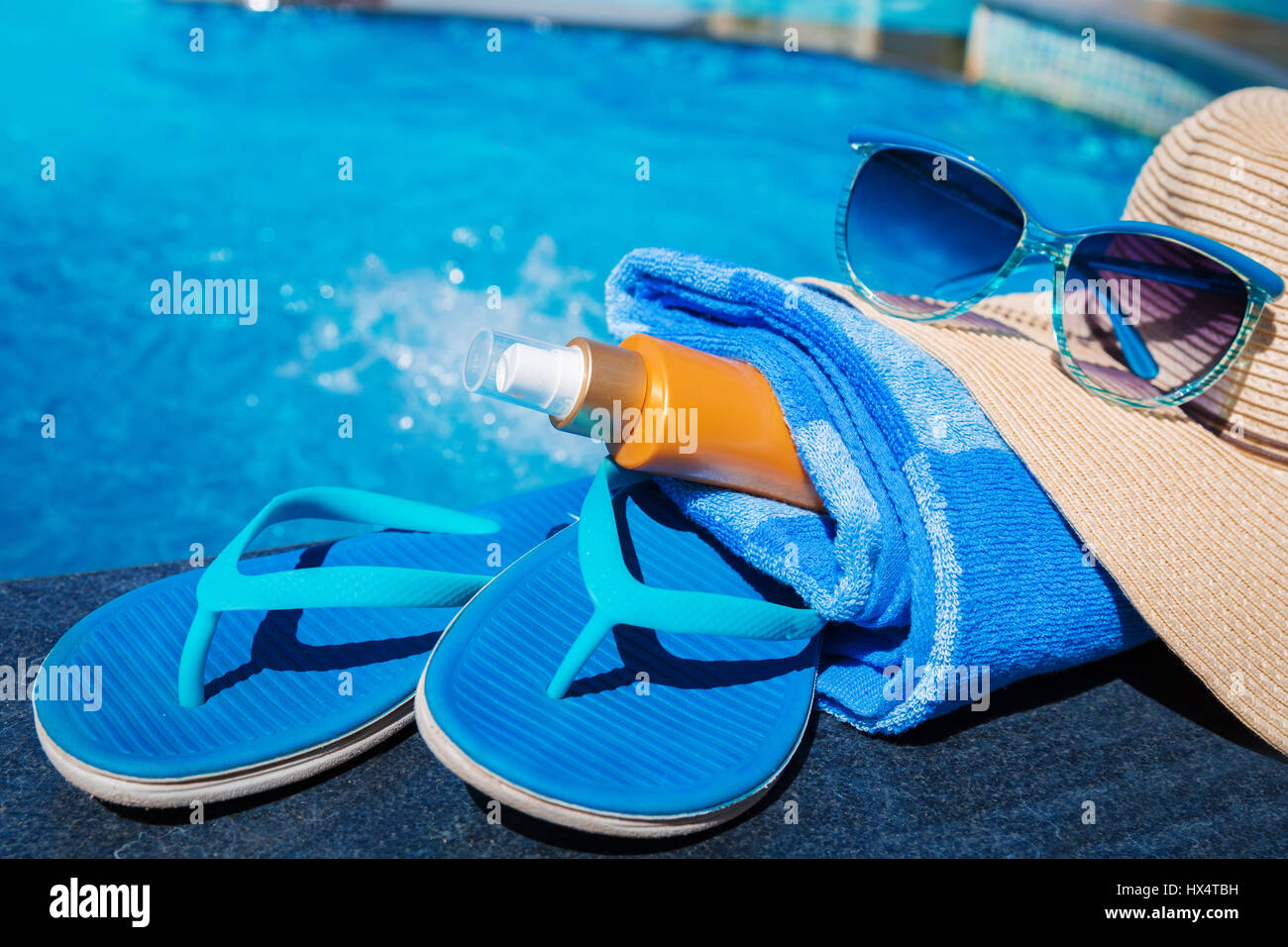 Pantofole blu con crema di protezione solare, asciugamano, cappello di paglia e gli occhiali da sole sul bordo di una piscina - vacanza concetto tropicale Foto Stock