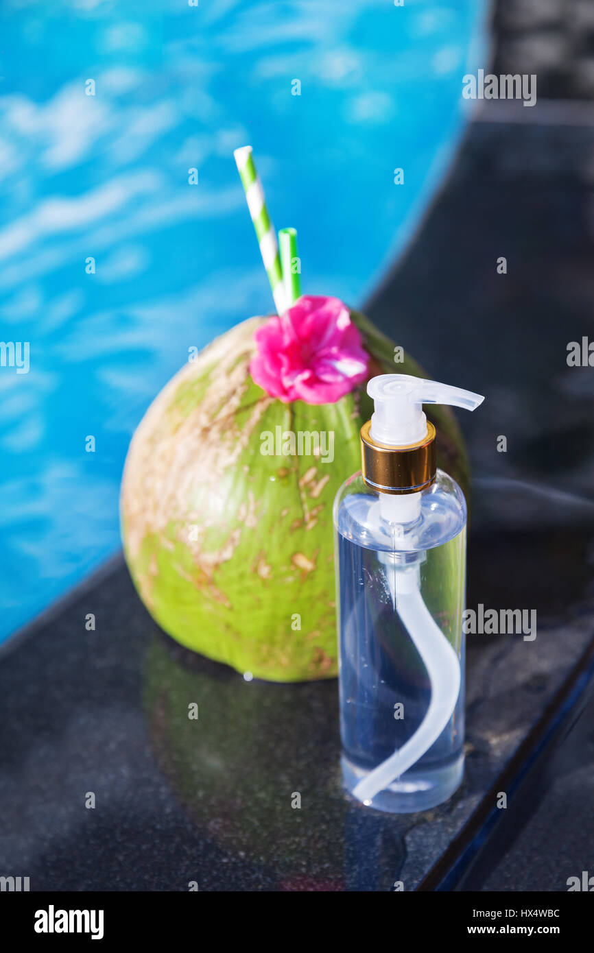 Succo di cocco drink con fiori e una bottiglia di olio sul bordo di una piscina - vacanza concetto tropicale Foto Stock