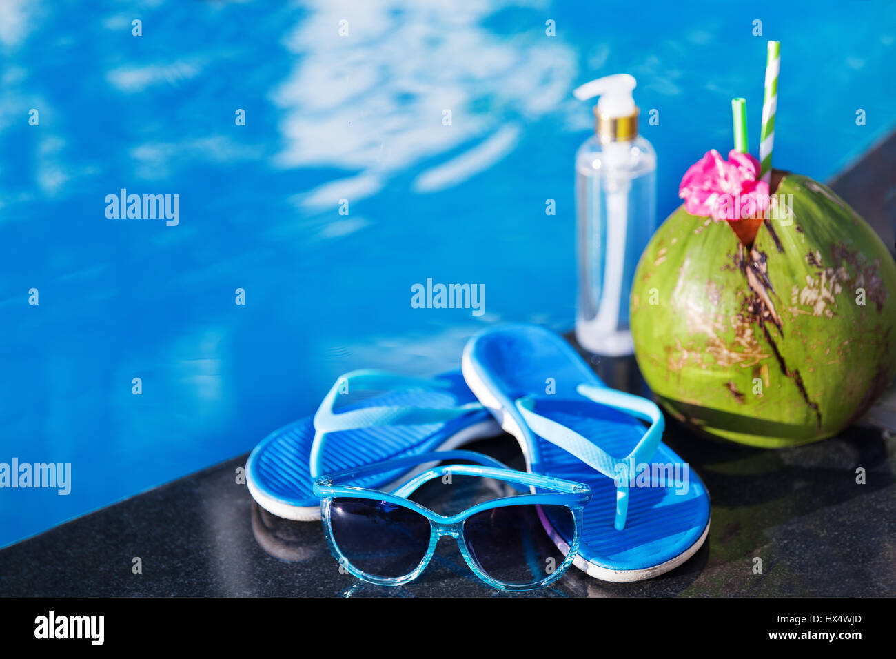 Olio di cocco del succo di frutta fresco smoothie cocktail drink di pantofole e occhiali da sole vicino alla piscina - estate salute Concetto di vacanza Foto Stock
