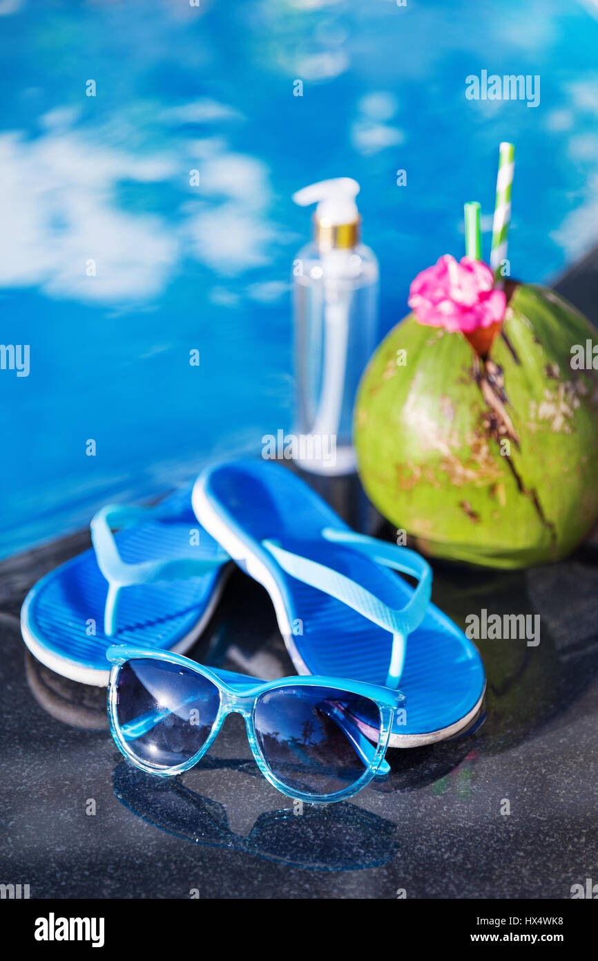 Olio di cocco del succo di frutta fresco smoothie cocktail drink di pantofole e occhiali da sole vicino alla piscina - estate salute Concetto di vacanza Foto Stock