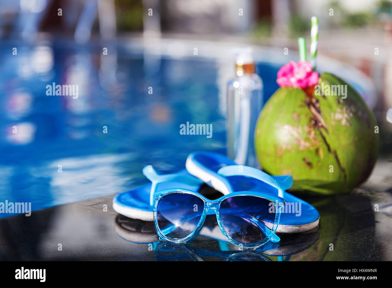 Il Cocco bere un succo con olio, pantofole e gli occhiali da sole sul bordo di una piscina - vacanza concetto tropicale Foto Stock
