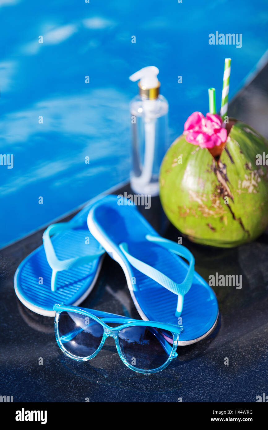 Olio di cocco del succo di frutta fresco smoothie cocktail drink di pantofole e occhiali da sole vicino alla piscina - estate salute Concetto di vacanza Foto Stock