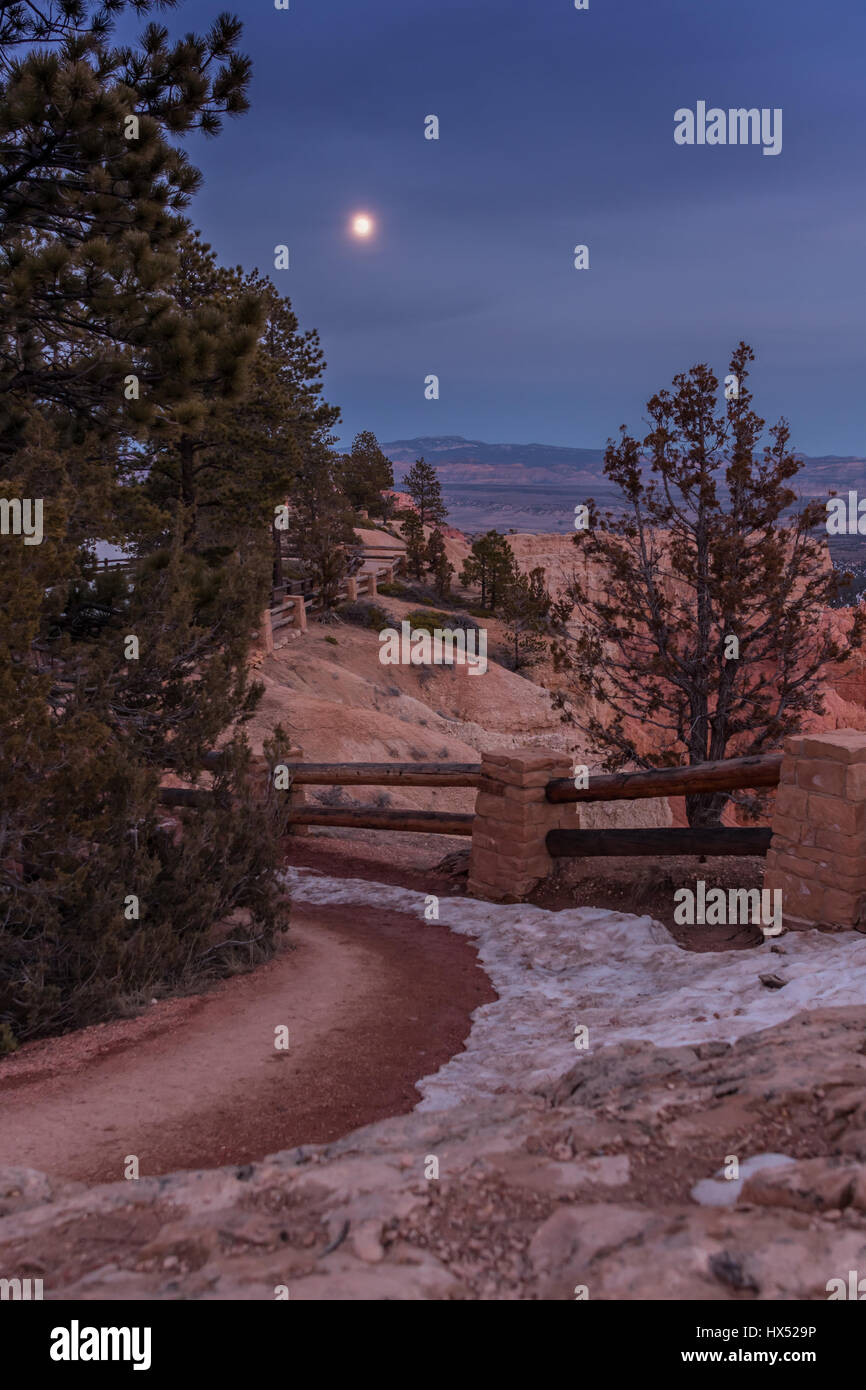 La luna sorge oltre il sentiero innevato al crepuscolo civile Foto Stock