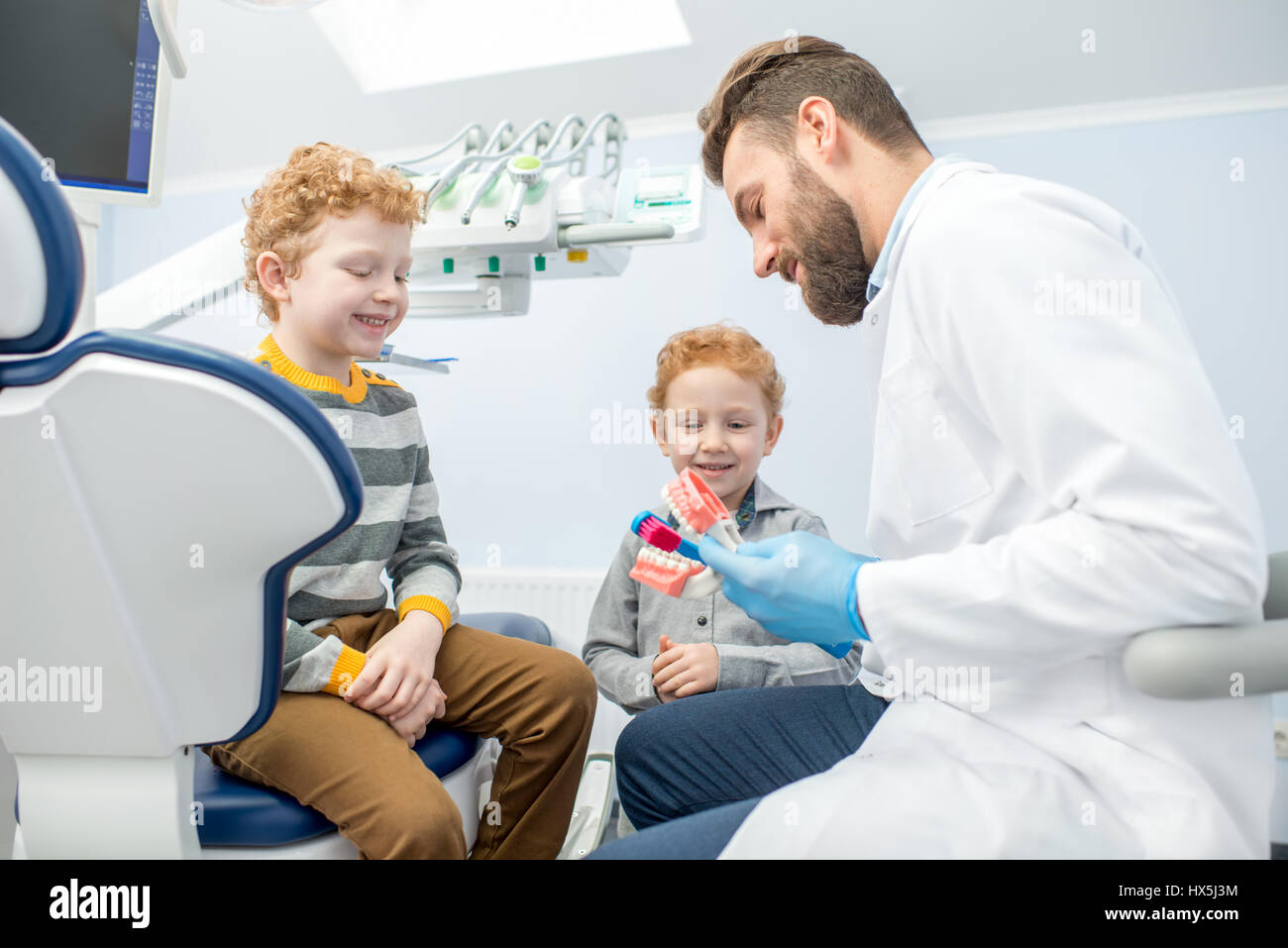 Bambini il dentista che mostra i ragazzi come spazzola denti sulla ganascia artificiale presso lo studio dentistico Foto Stock