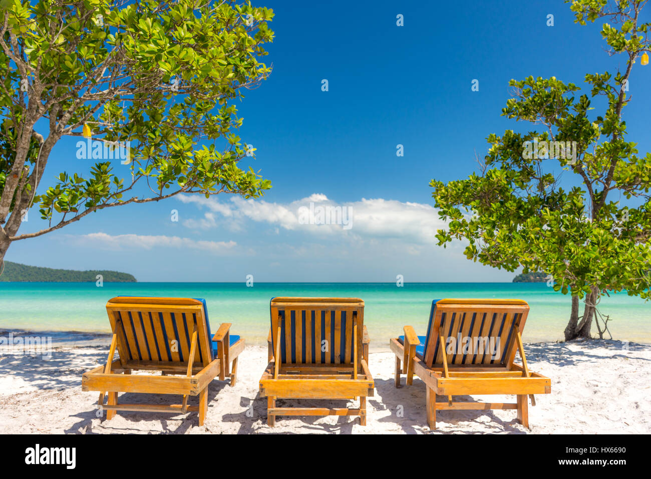 Tre lettini per prendere il sole su una spiaggia di sabbia bianca che guarda ad una tranquilla vuoto mare tropicale. Angolo basso. Foto Stock