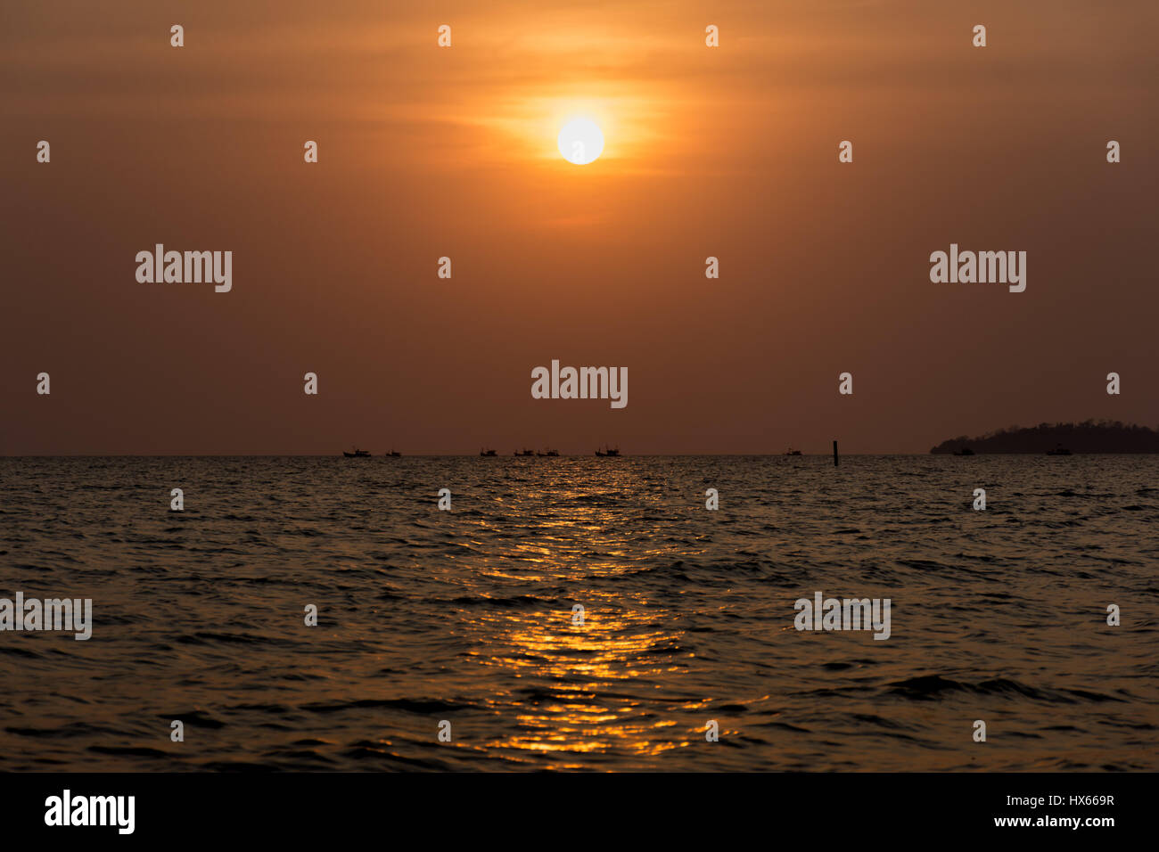 Il sole tramonta come una flottiglia di pescherecci testa fuori al mare. Foto Stock