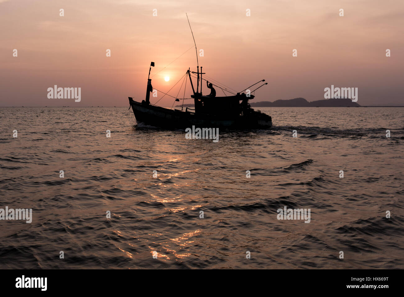 Un vecchio legno barca da pesca capi al mare come il sole tramonta dietro di esso. Foto Stock