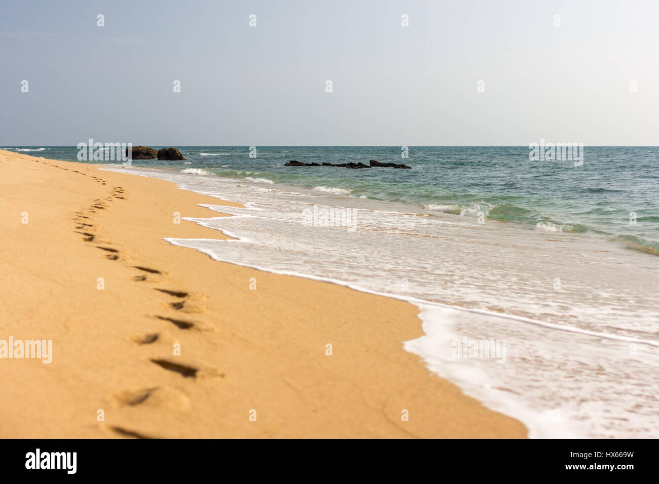 Una linea di piede di stampe in una spiaggia di sabbia dorata con acqua di mare arrivando fino alla spiaggia. Foto Stock