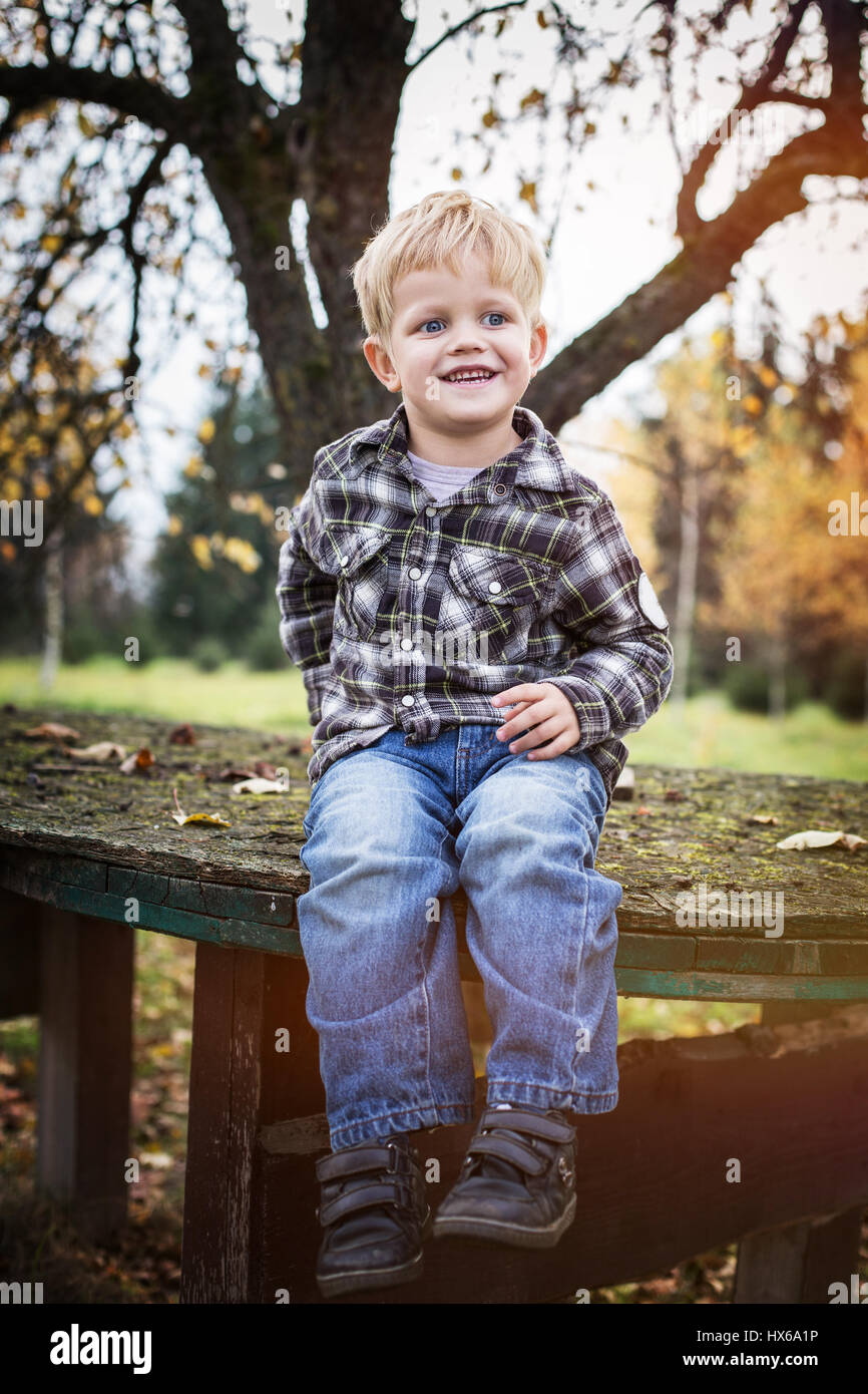 Bella bionda casual bambino seduto all'esterno sul tavolo e ridere. L'autunno. Ritratto all'aperto Foto Stock