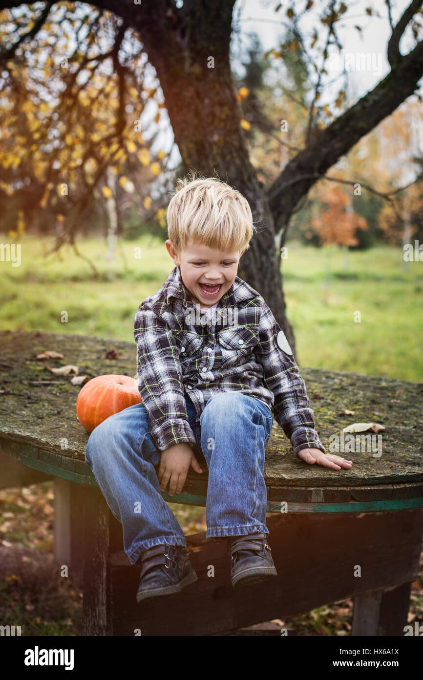 Bella bionda casual bambino seduto all'esterno sul tavolo e ridere. L'autunno. Ritratto all'aperto Foto Stock