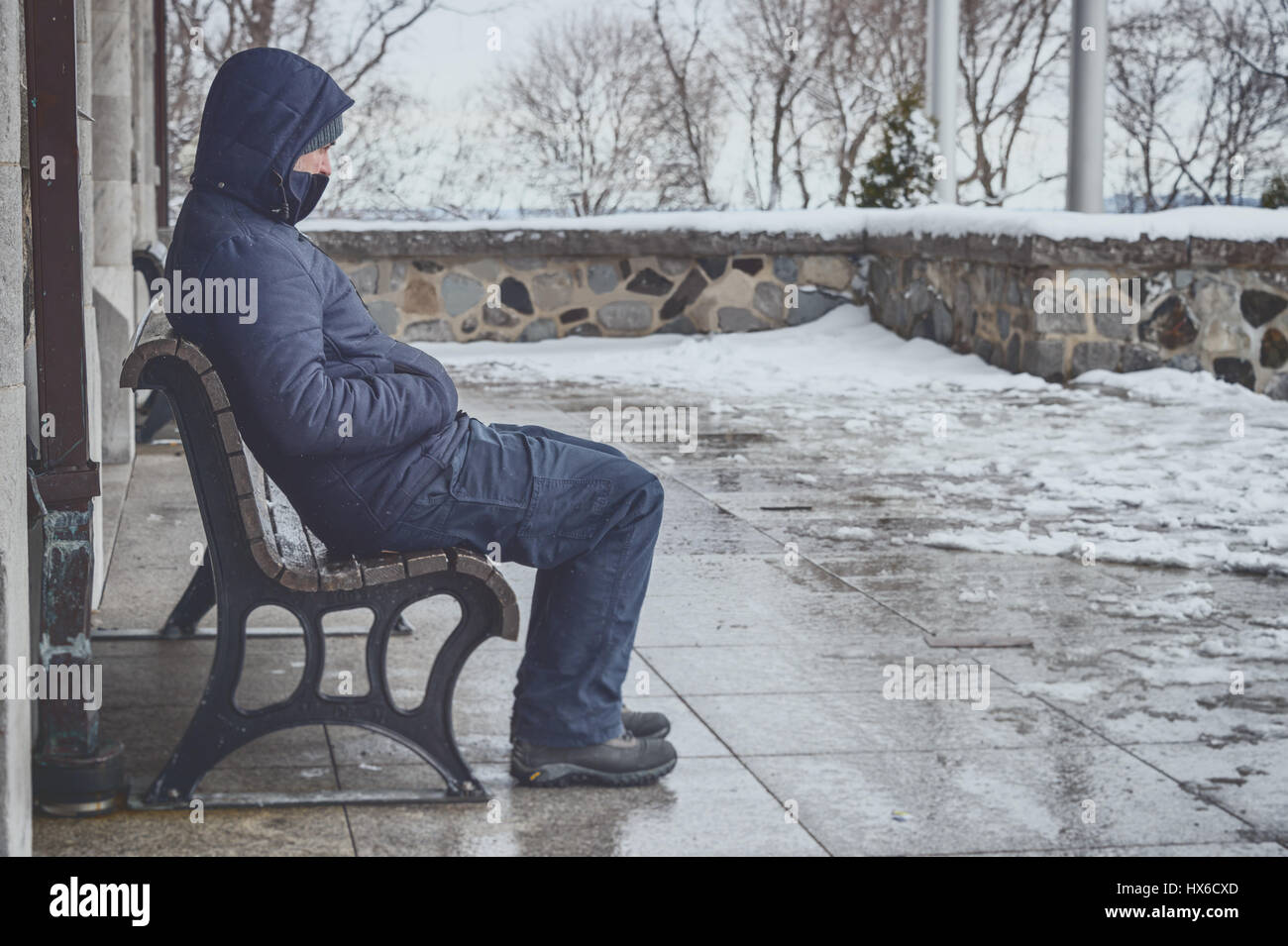 Uomo seduto su un banco in inverno con neve sul terreno Foto Stock