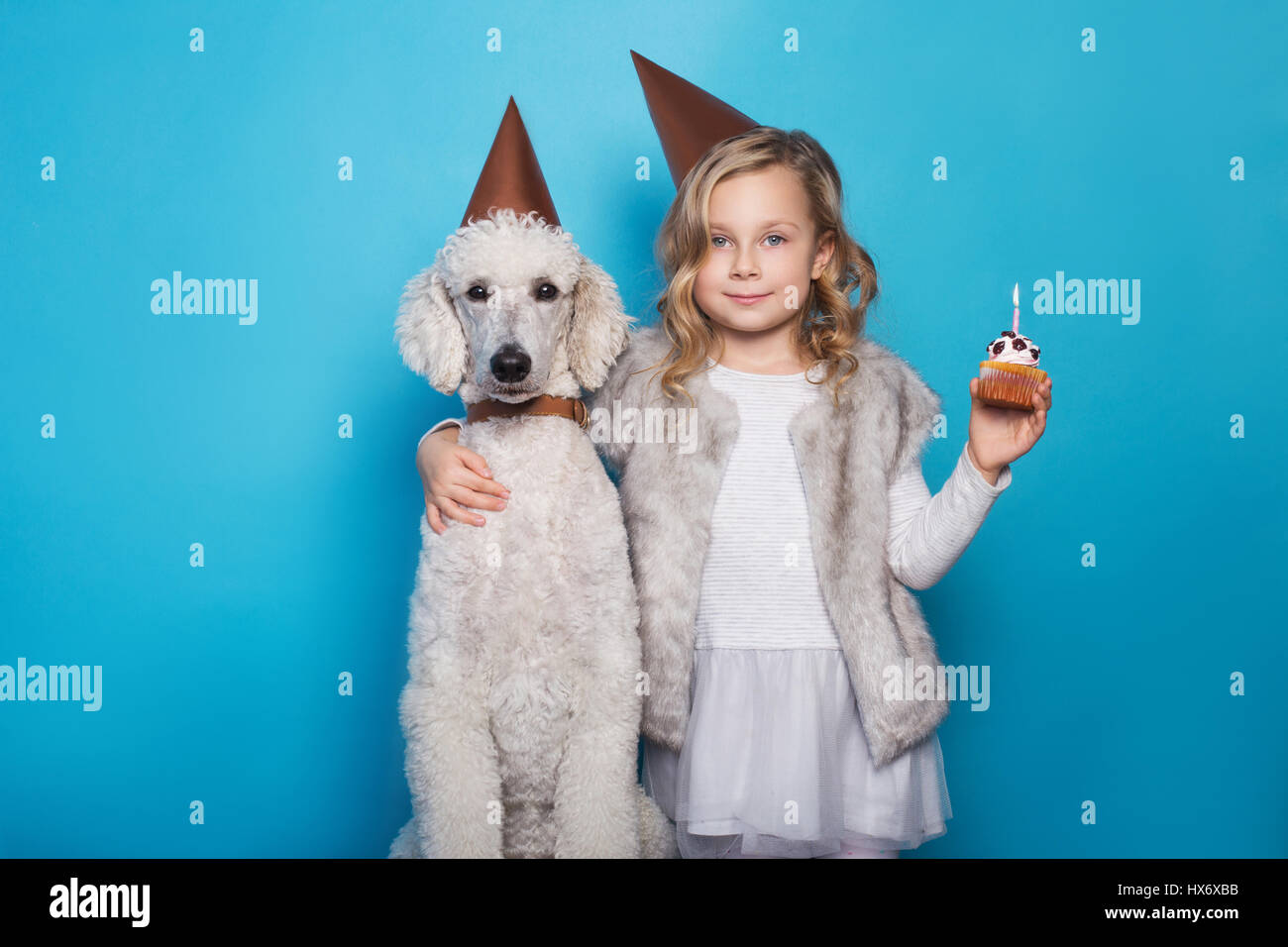 Poco bellissima ragazza con cane festeggiare il compleanno. L'amicizia. L'amore. La torta con la candela. Ritratto in studio su sfondo blu Foto Stock