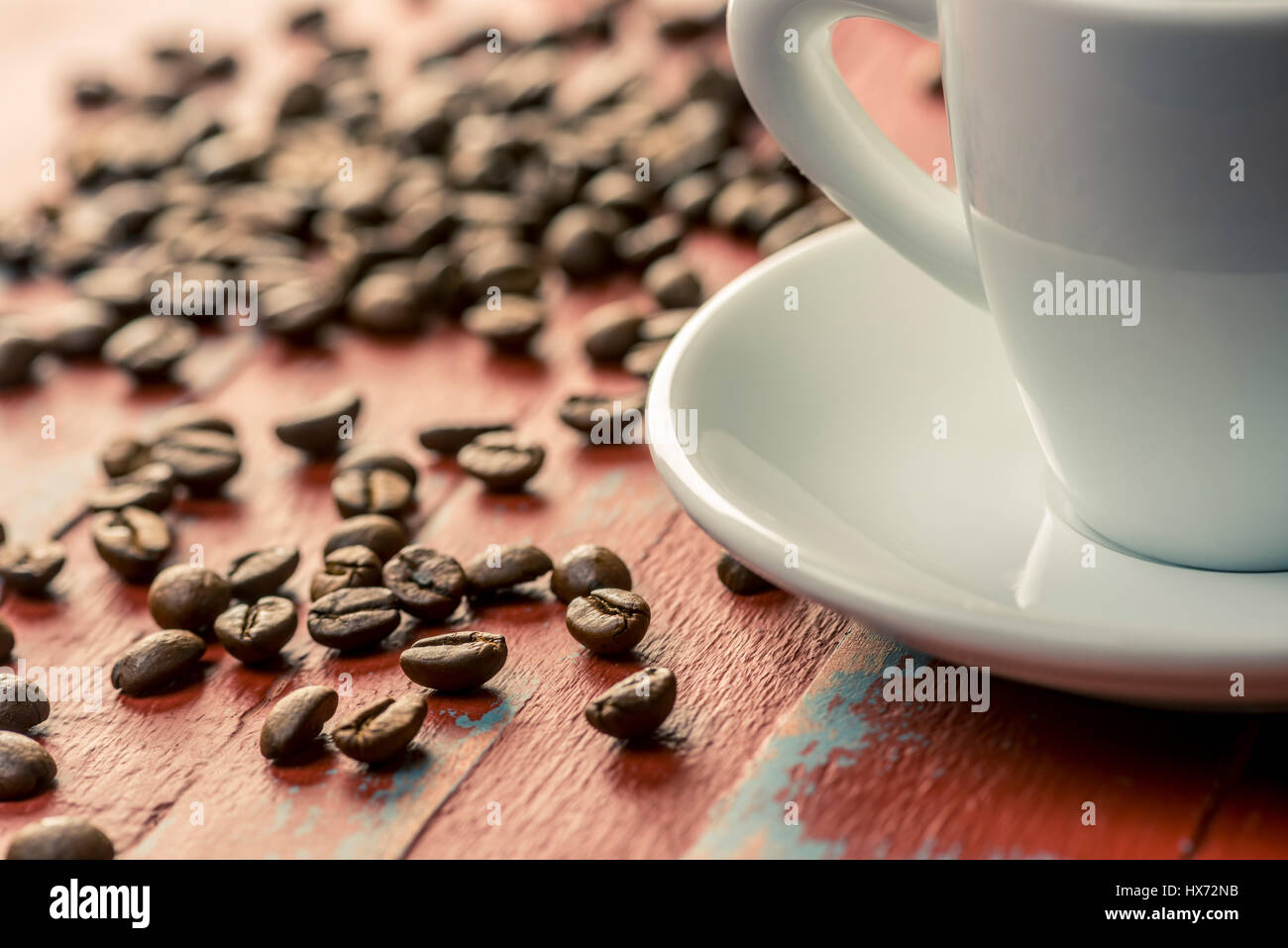 Chicchi di caffè tostati dipinto su tavola di legno con il bianco tazzina e piattino Foto Stock