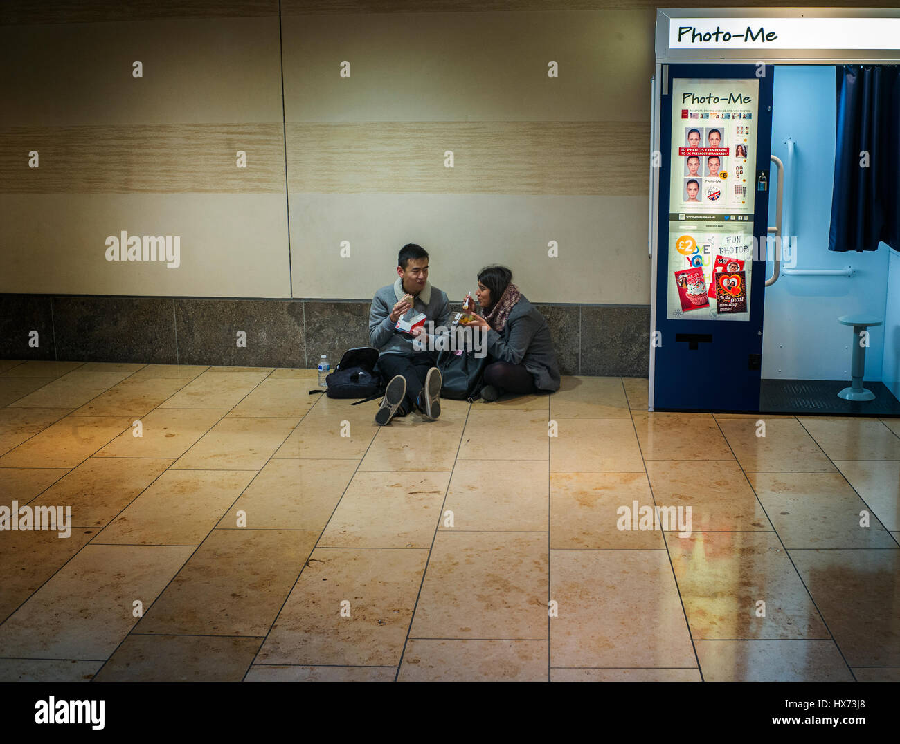 Due persone mangiare il pranzo sul pavimento accanto a una foto-me istant Photo Booth in Cambridge shopping centre Foto Stock