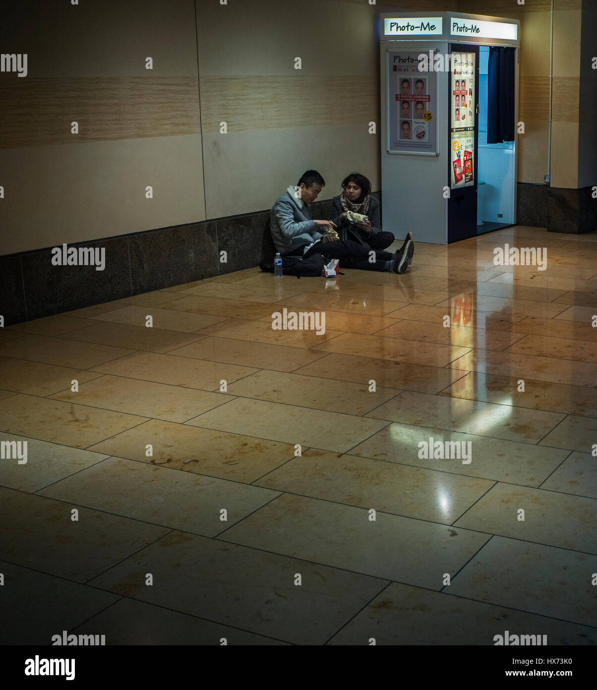 Due studenti di mangiare picknick sul pavimento accanto a una foto-me istant Photo Booth in Cambridge shopping centre Foto Stock