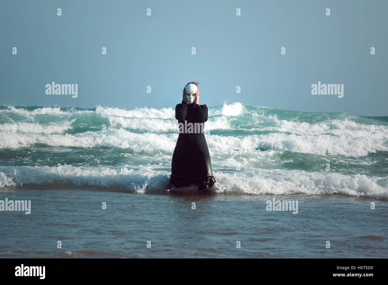 Donna in abito nero con maschera, in piedi il surf in mare Foto Stock