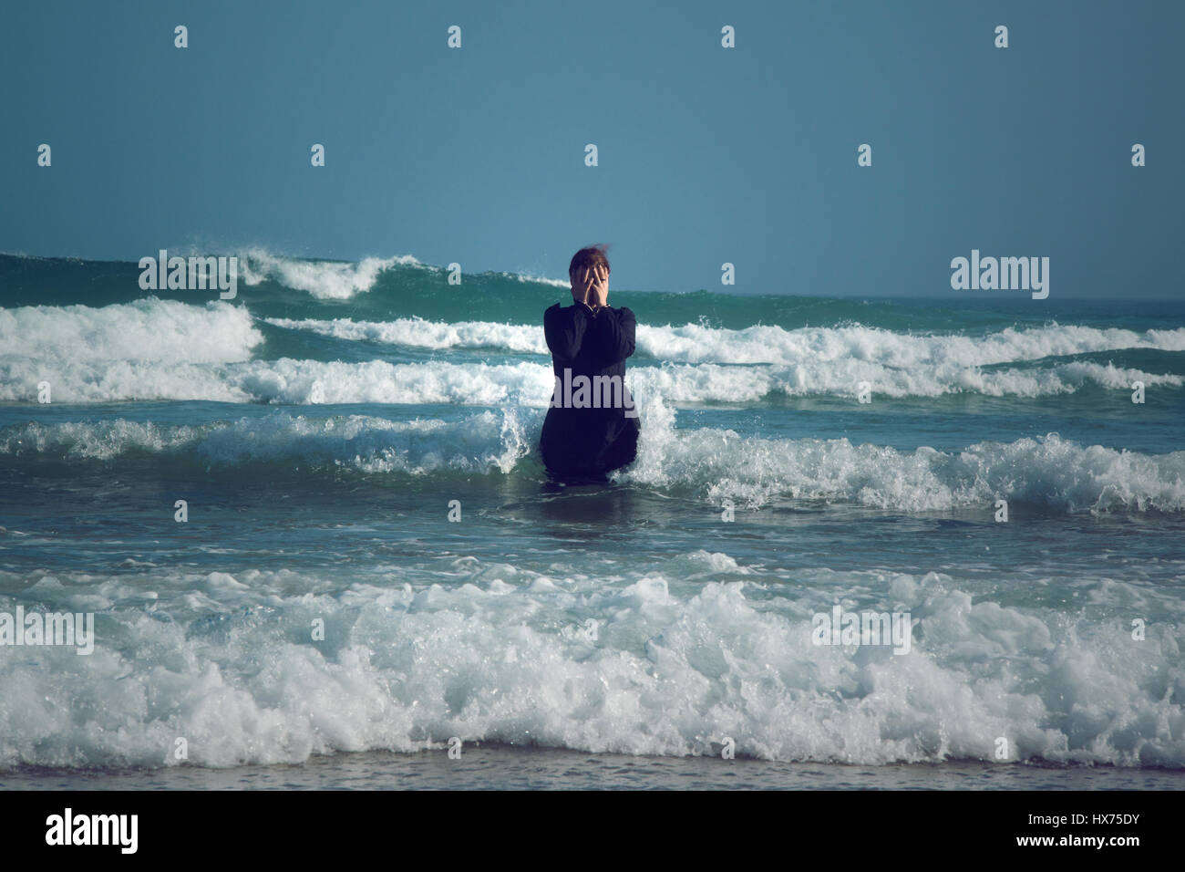 Donna in abito nero con maschera, in piedi il surf in mare Foto Stock
