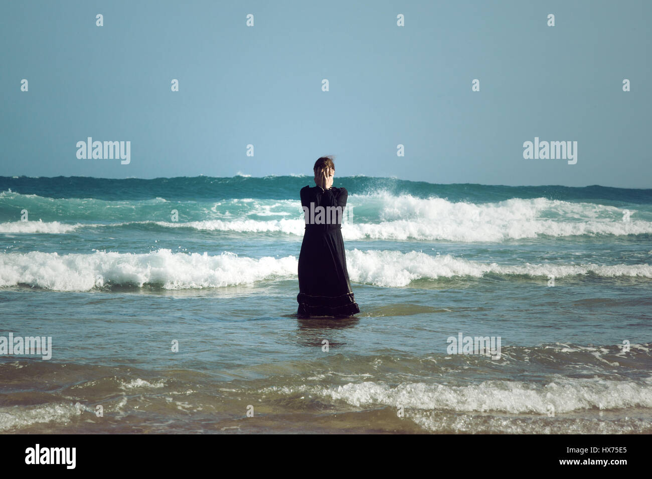 Donna in abito nero con maschera, in piedi il surf in mare Foto Stock