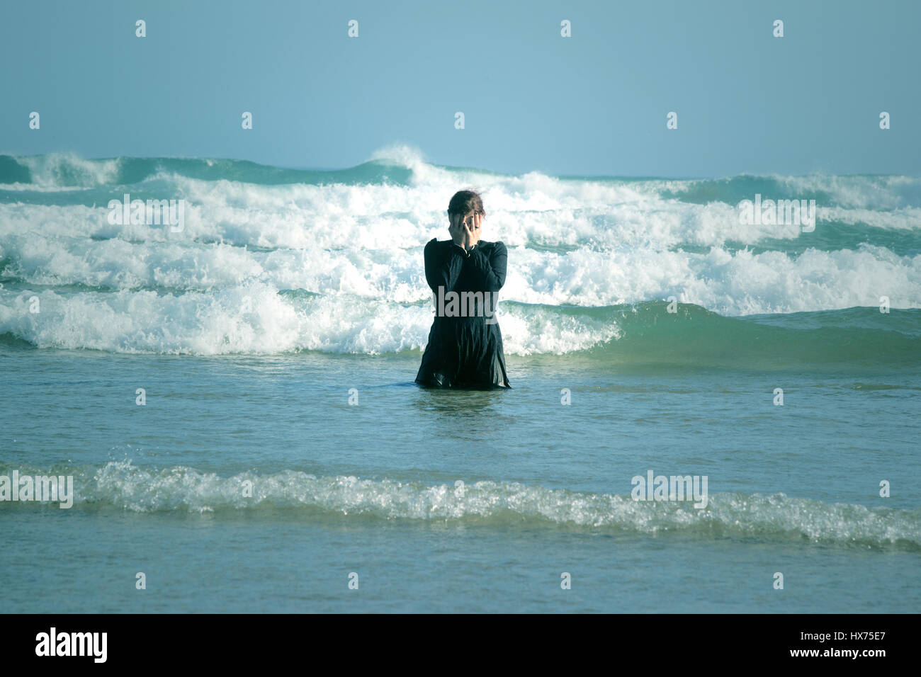 Donna in abito nero con maschera, in piedi il surf in mare Foto Stock