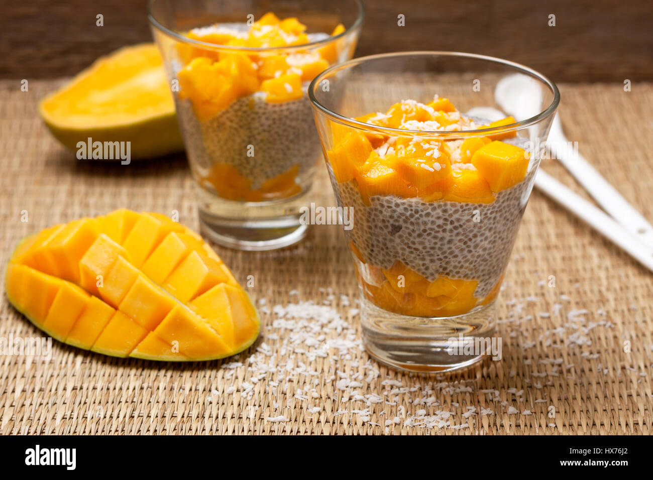 Una sana prima colazione. Budino di Chia con mango in bicchieri di vetro, mezza mango su un sfondo di paglia. Messa a fuoco selettiva Foto Stock