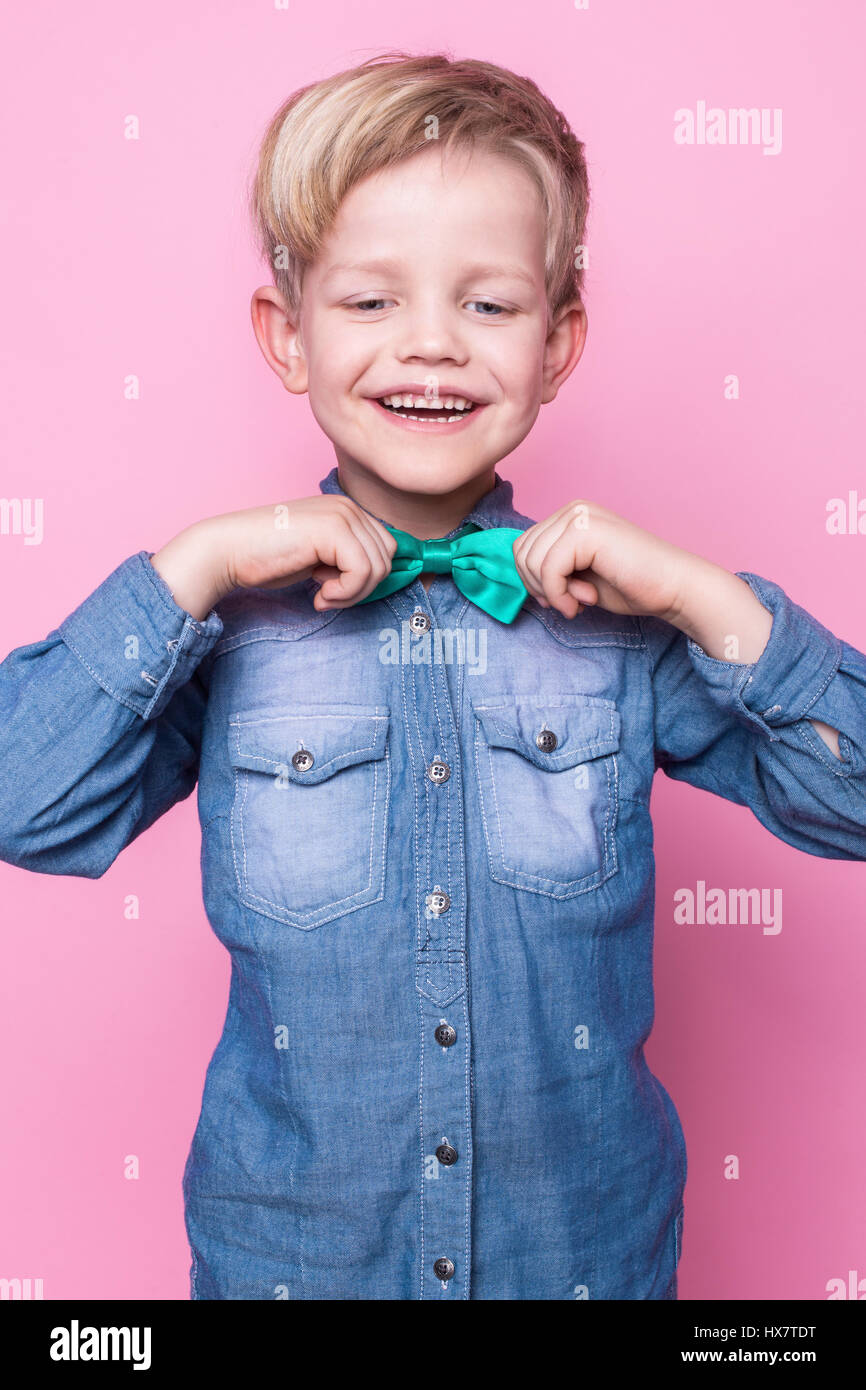 Giovani bel ragazzo con la maglietta blu e cravatta a farfalla. Moda. Modello. Ritratto in studio su sfondo rosa Foto Stock