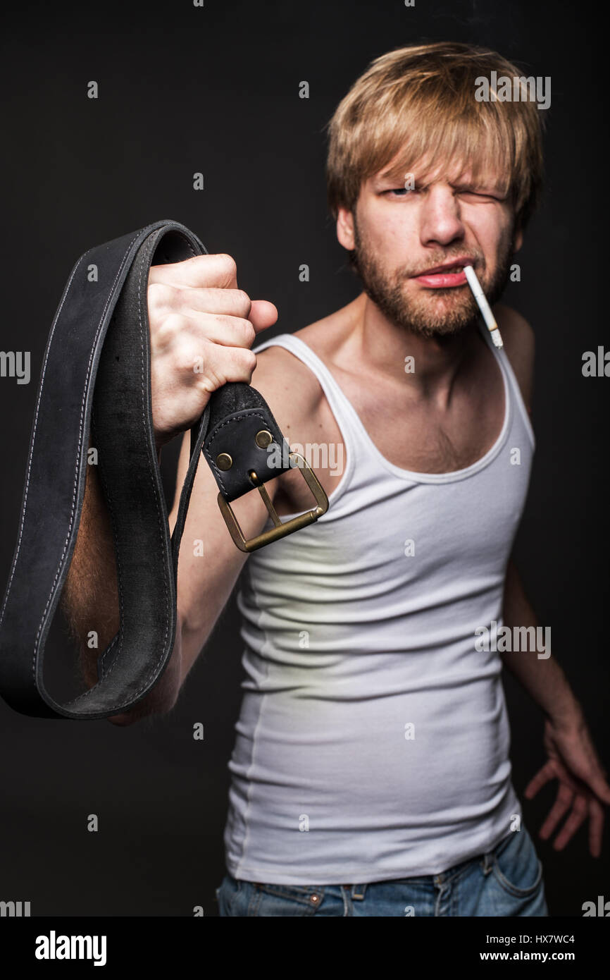 L'uomo arrabbiato minaccia con la cinghia. Concetto: la violenza contro le donne. Ritratto in studio su sfondo nero Foto Stock