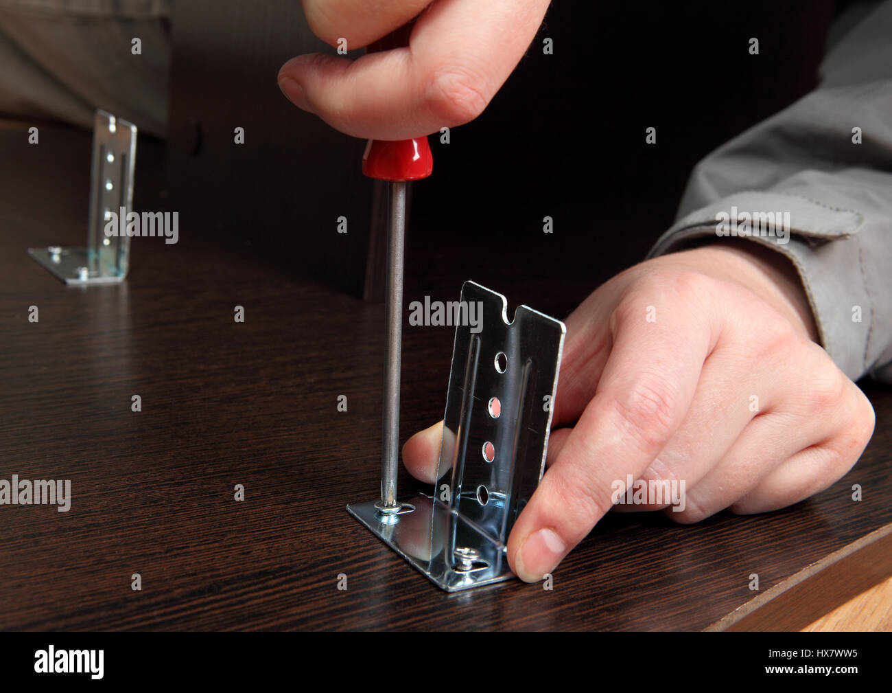 Montaggio di mobili a mano, close-up, cacciavite, avvitando la vite che fissa la staffa di metallo sulle guide di scorrimento del vassoio della tastiera computer desk. Foto Stock