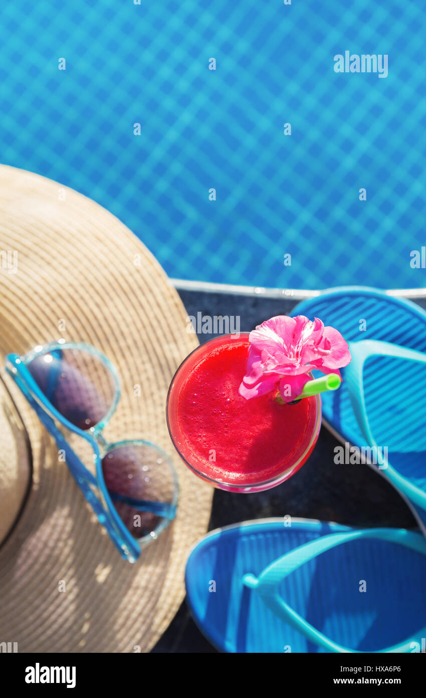 Acqua melone rosso succo fresco drink smoothie cocktail pantofole, cappello di paglia e occhiali da sole vicino alla piscina Foto Stock