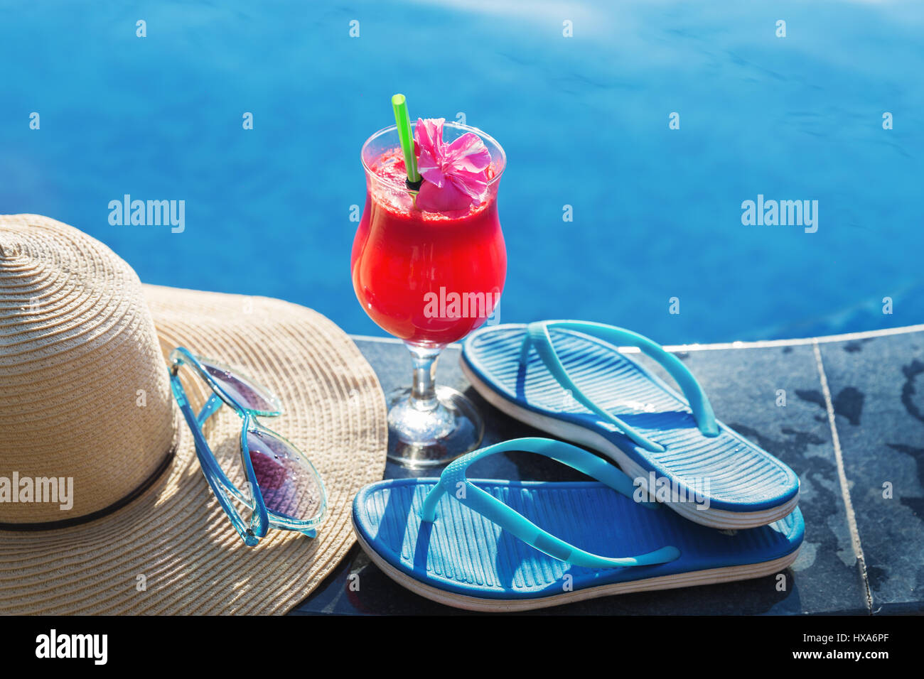 Anguria succo fresco drink frullato di vetro con fiori, occhiali da sole, pantofole e cappello di paglia sul bordo di una piscina - vacanza concetto tropicale Foto Stock