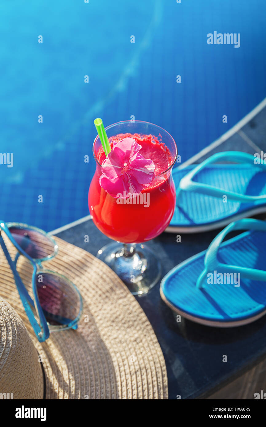 Anguria succo fresco drink frullato di vetro con fiori, occhiali da sole, pantofole e cappello di paglia sul bordo di una piscina - vacanza concetto tropicale Foto Stock
