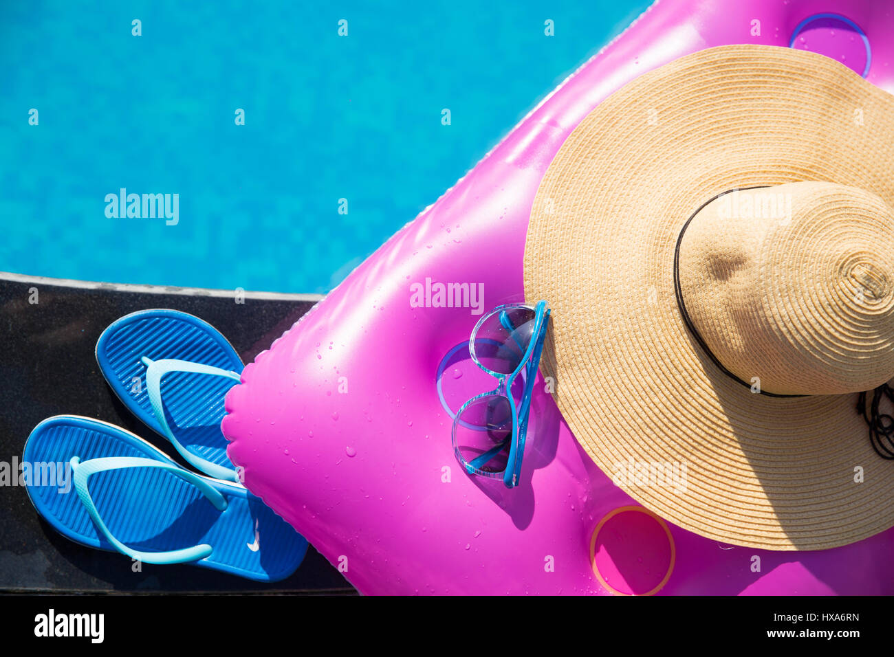 Blue pantofole, occhiali da sole e cappello di paglia e rosa aria materasso sul bordo di una piscina - vacanza concetto tropicale Foto Stock