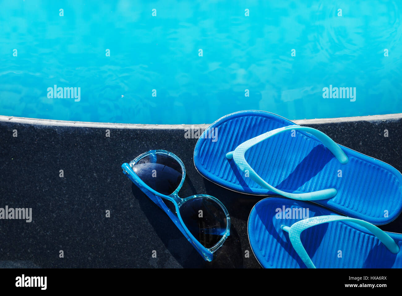Pantofole blu e gli occhiali da sole sul bordo di una piscina - vacanza concetto tropicale Foto Stock