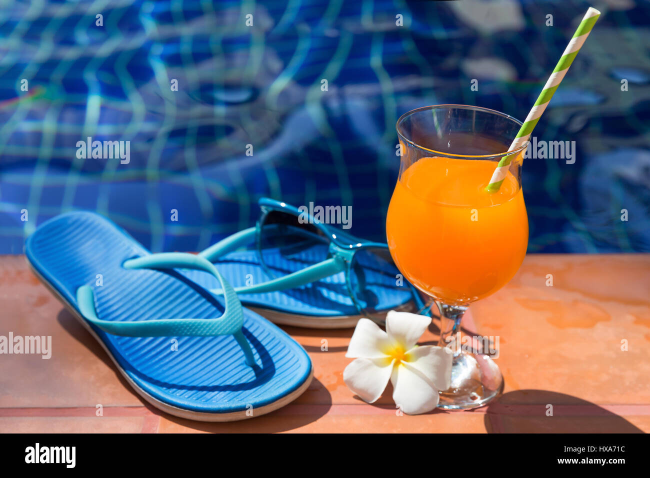 Orange mango succo di frutta fresco smoothie cocktail drink di pantofole e occhiali da sole vicino alla piscina - vacanza estiva concept Foto Stock
