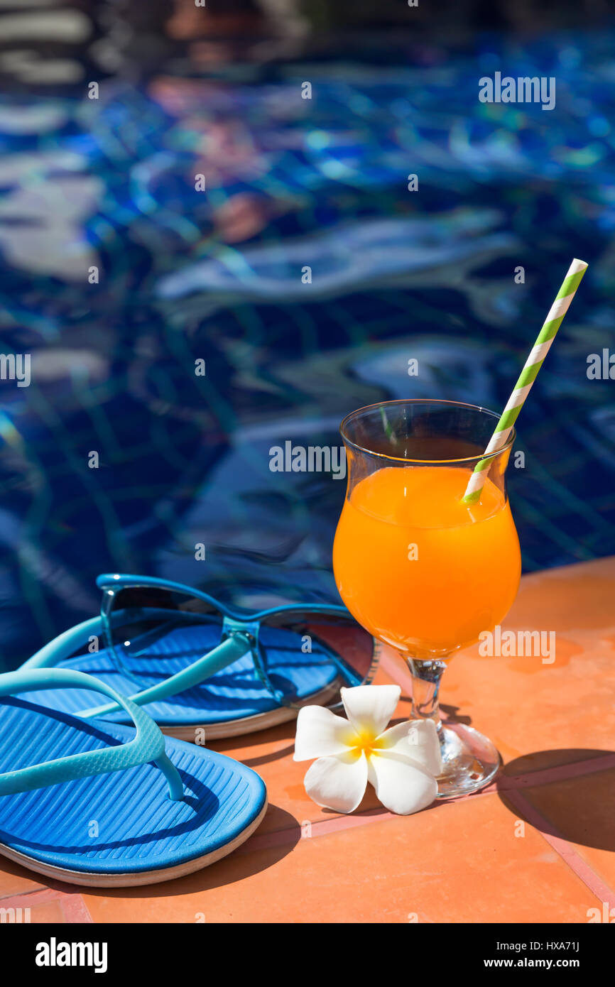 Orange mango succo di frutta fresco smoothie cocktail drink di pantofole e occhiali da sole vicino alla piscina - vacanza estiva concept Foto Stock