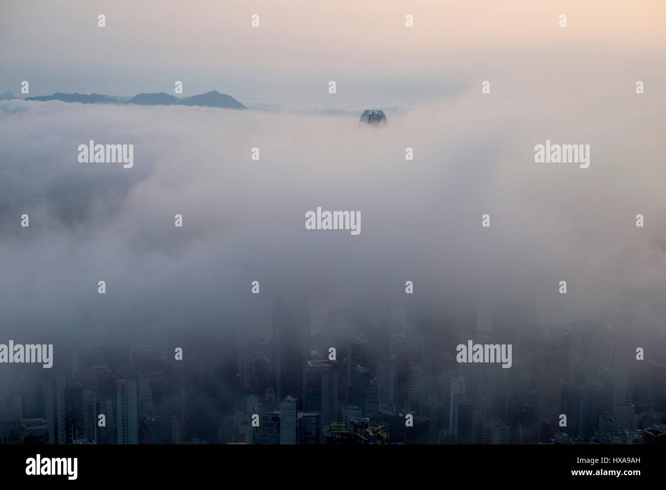 Lo skyline della città è coperto di nuvole basse e nebbia di mare durante il tramonto visto attraverso il Victoria Harbour a Hong Kong, Cina. Foto Stock