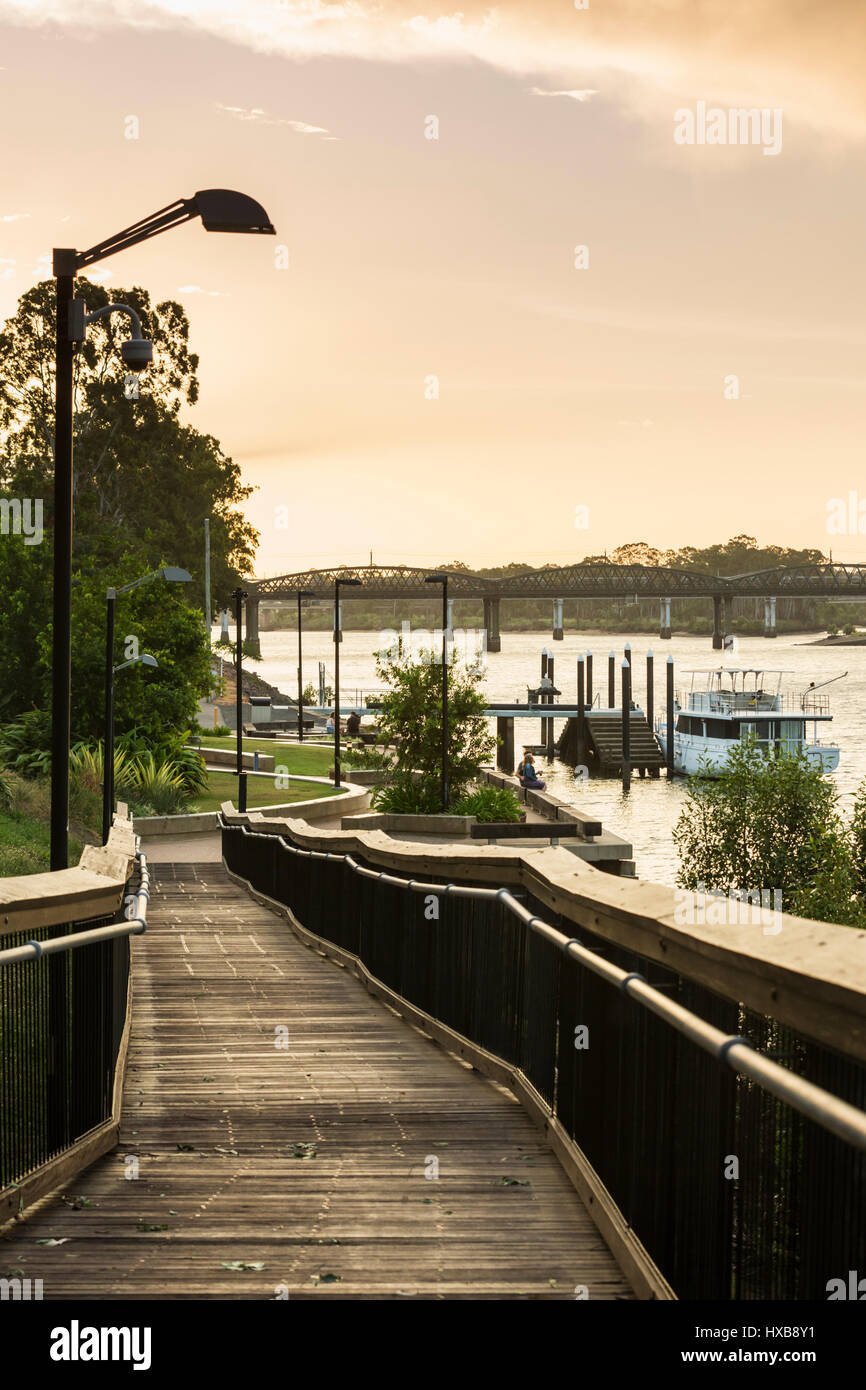 Vista lungo la passeggiata lungo il fiume al tramonto con il ponte di Burnett in distanza. Bundaberg, Queensland, Australia Foto Stock