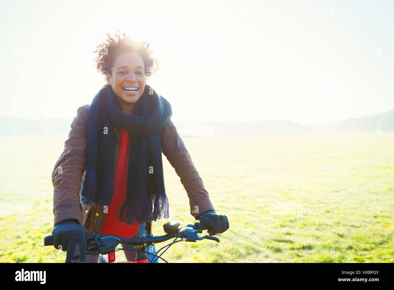 Donna sorridente in bicicletta nel soleggiato parco erba Foto Stock