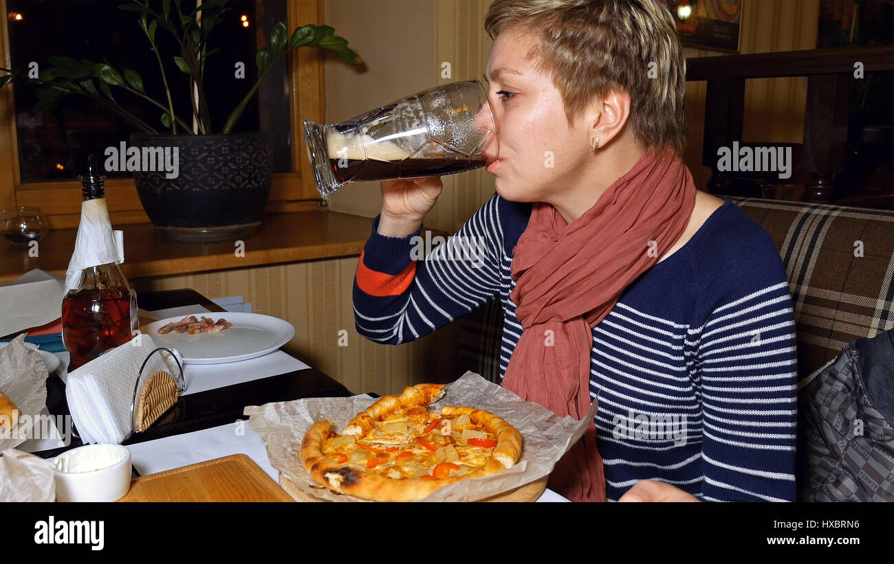 Bella donna bionda mangia la pizza e bevande birra Foto Stock