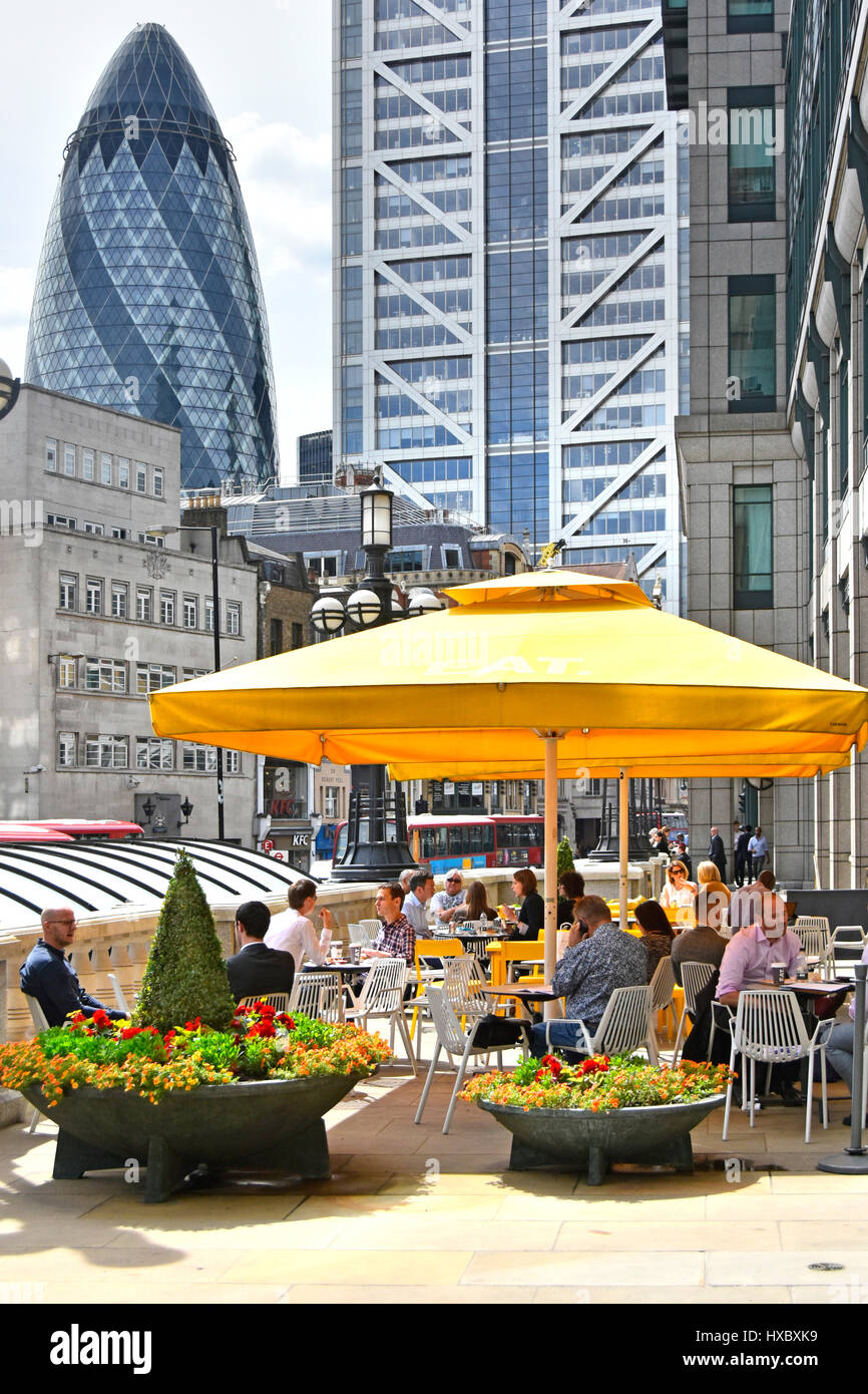 Persone mangiare il pranzo tempo snacking all'aperto a mangiare sandwich shop con il Gherkin & Heron grattacielo Torre al di là dei punti di riferimento della città di Londra REGNO UNITO Foto Stock