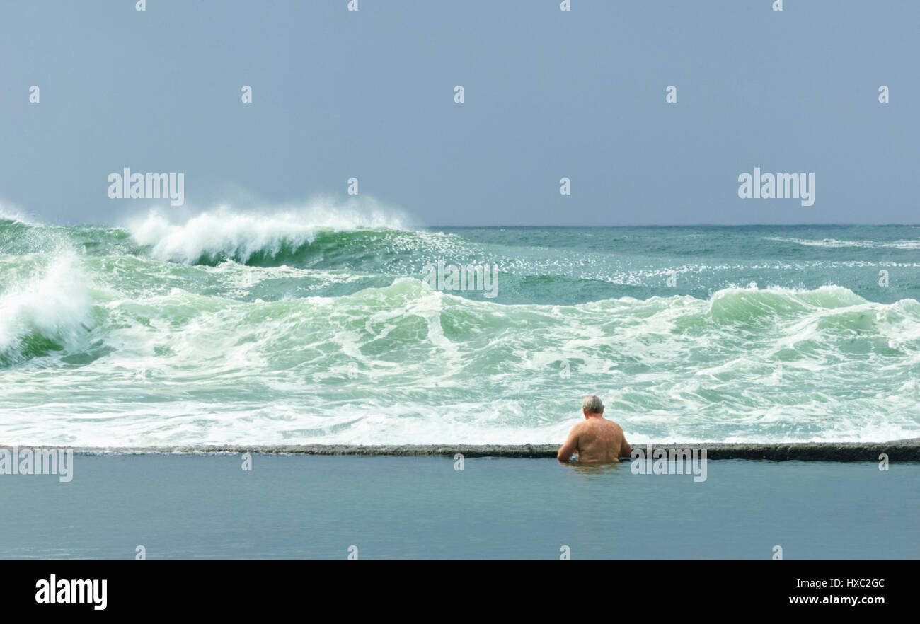 L'uomo contemplando il mare agitato con grandi onde dal rock pool, Gerringong, Illawarra Costa, Nuovo Galles del Sud, NSW, Australia Foto Stock