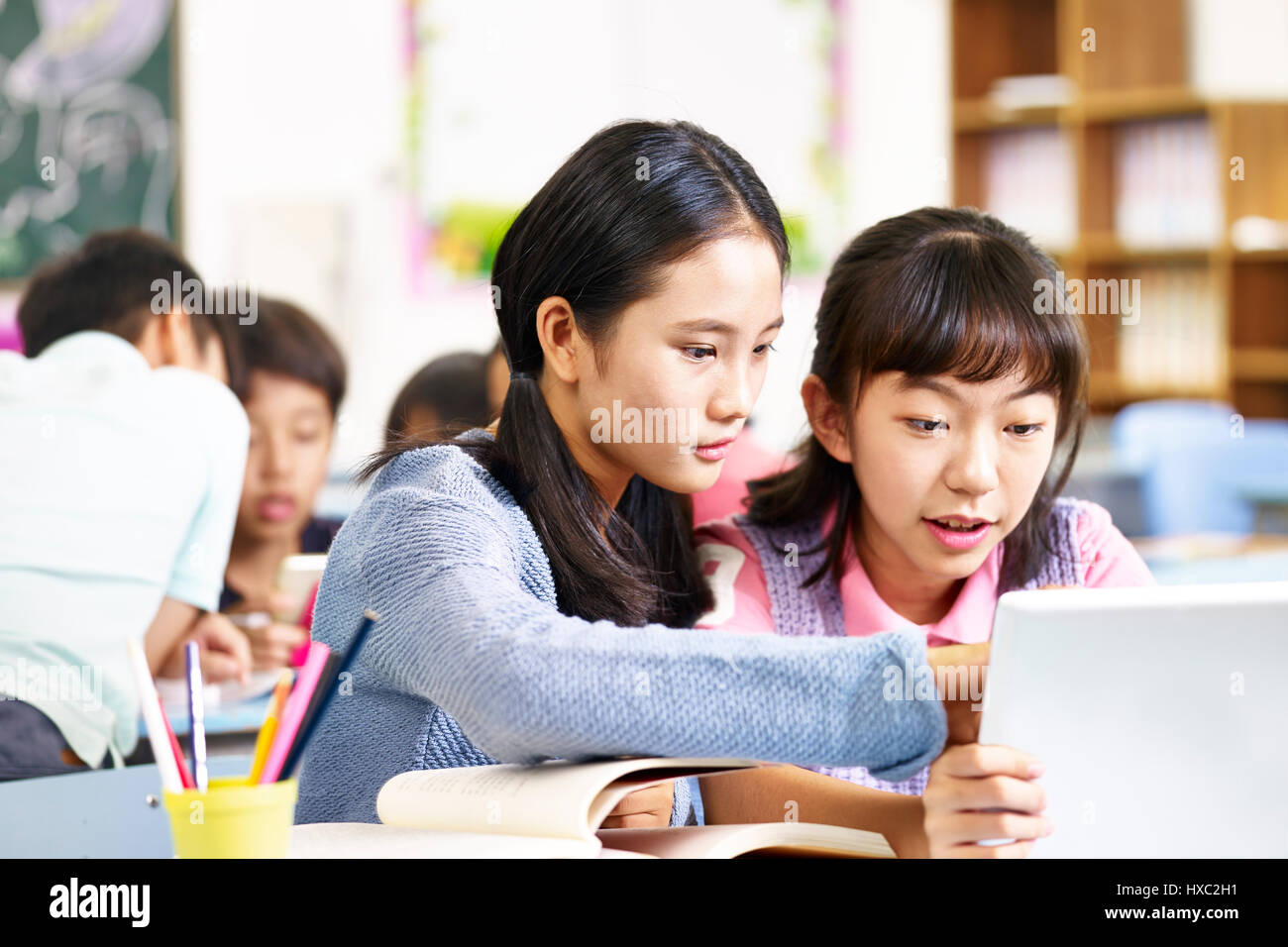 Due asian scuola elementare ragazze utilizzando computer tavoletta mentre si lavora in gruppo. Foto Stock