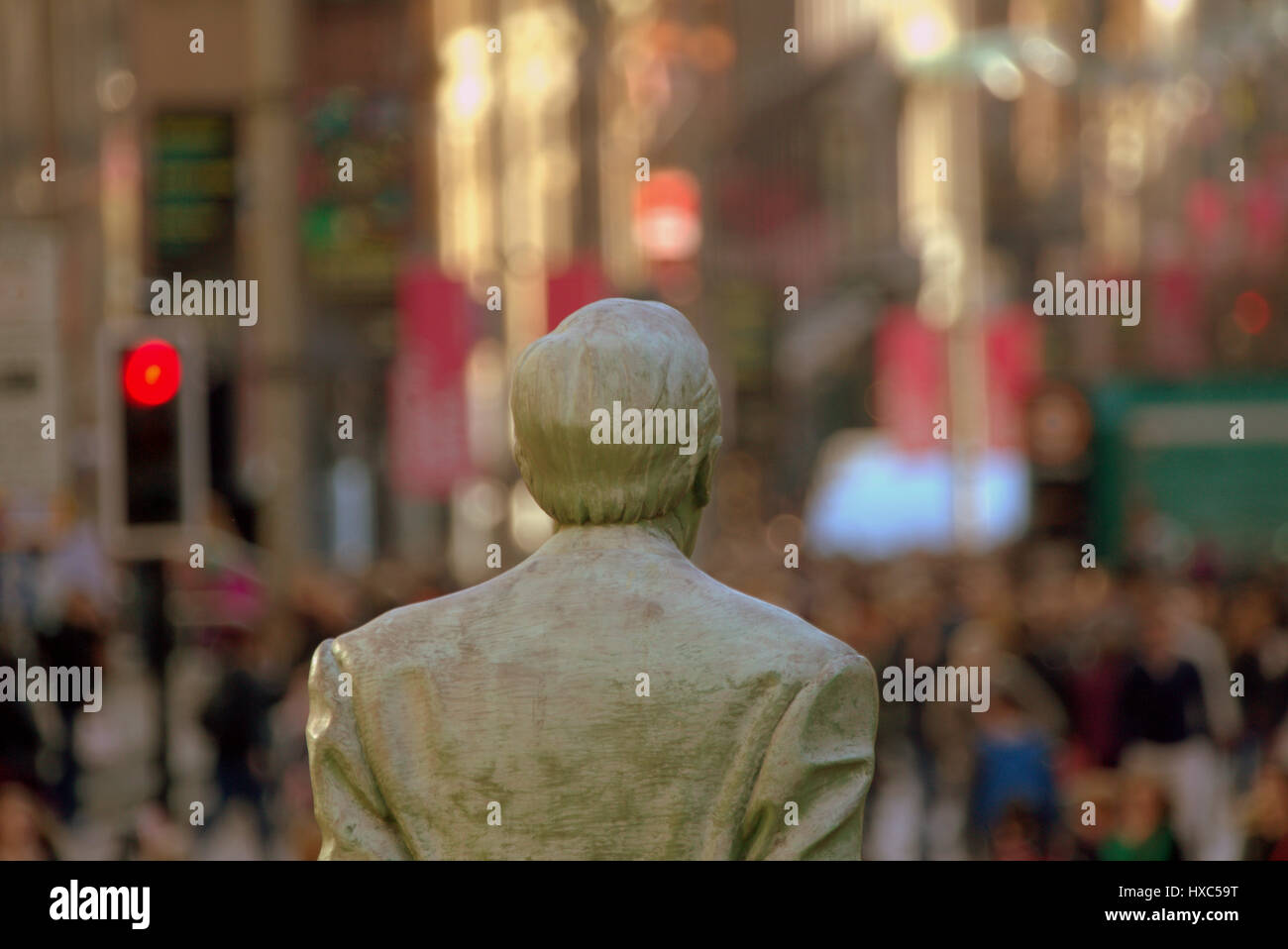 Testa posteriore colpo di Donald Dewar statua come egli guarda un bokeh Glasgow con un segno di stop rosso Foto Stock