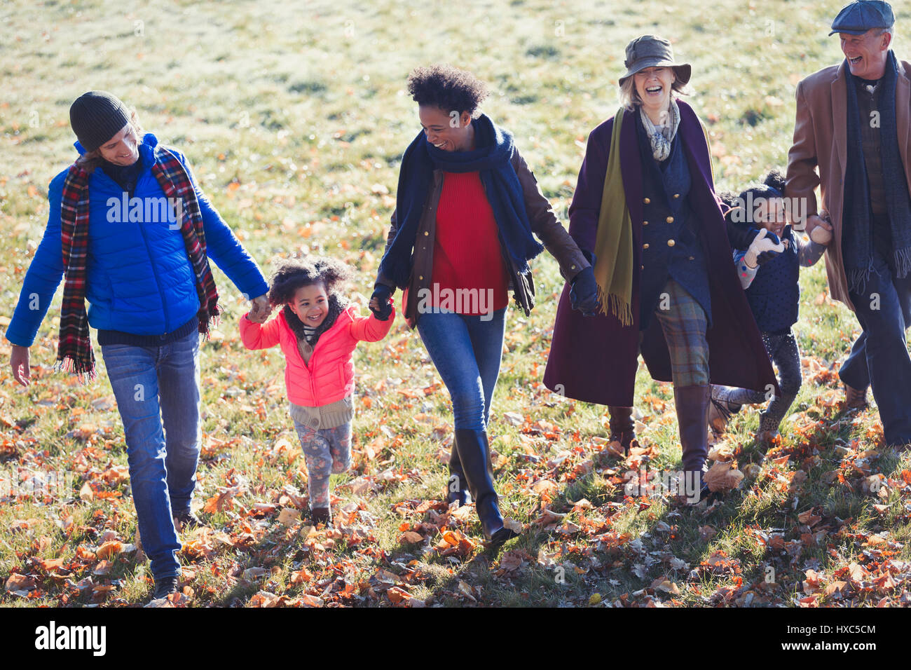 Multi-generazione famiglia tenendo le mani e piedi nel soleggiato parco di autunno Foto Stock