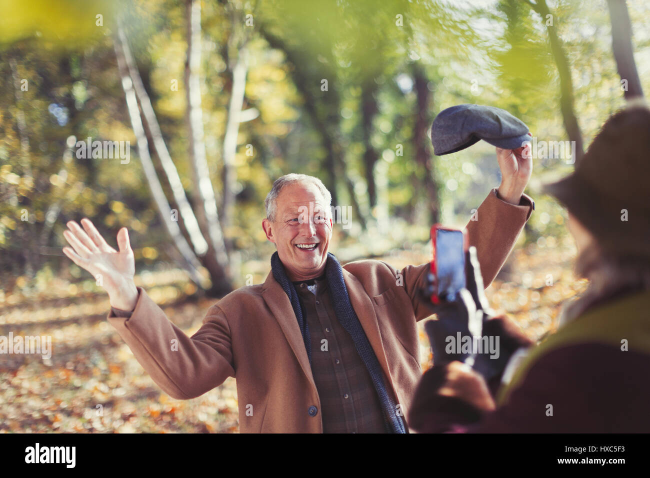 Uomo Senior in posa per moglie con la fotocamera del telefono in autunno park Foto Stock