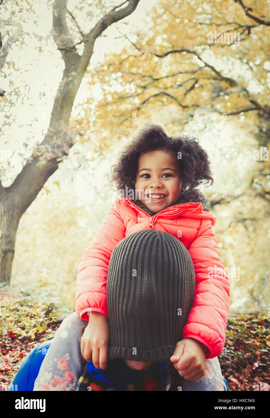 Ritratto sorridente figlia tirando calza cappuccio sulla testa dei padri in autunno park Foto Stock