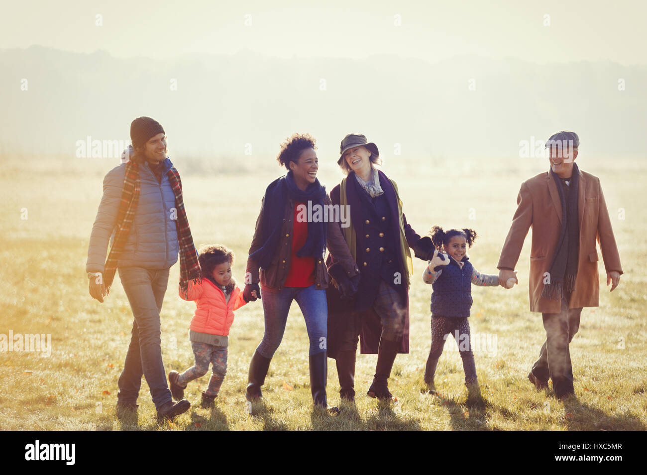 Multi-generazione famiglia tenendo le mani a piedi nella soleggiata erba di autunno Foto Stock