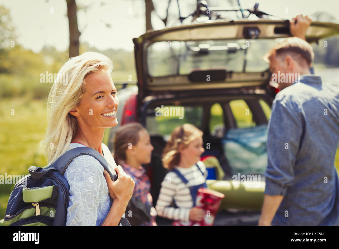 Donna sorridente con zaino preparando per escursione con la famiglia al di fuori auto Foto Stock