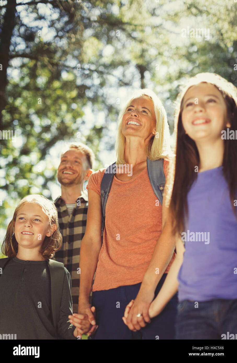 Famiglia sorridente holding hands escursioni nei boschi di sole Foto Stock