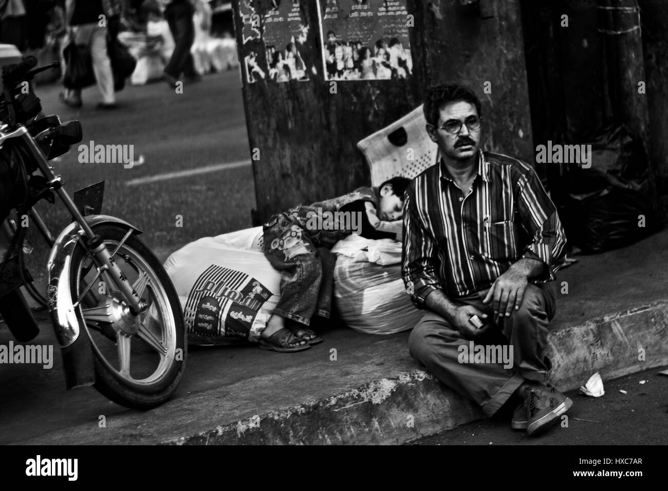 Un egiziano uomo seduto vicino alla strada mentre un bambino di strada sta dormendo dietro di lui. Foto Stock