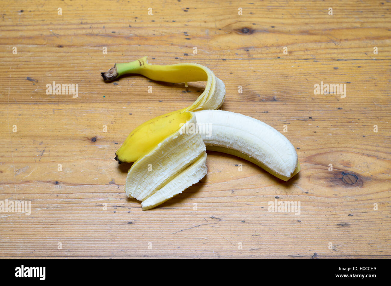 Parzialmente pelato uneaten tutta la banana matura giacente al centro di un tavolo di legno circondato da spazio di copia in un concetto di sana alimentazione e nutrizione Foto Stock